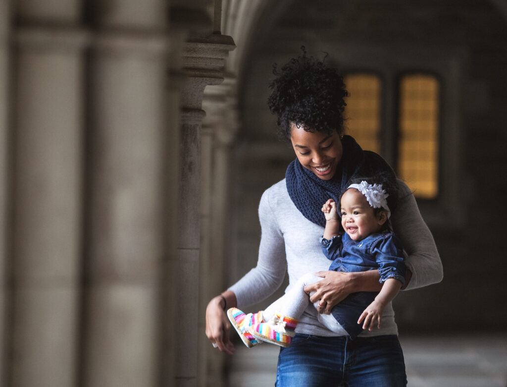 Mother holding her child outdoors in front of a stone archway